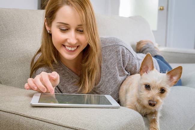 Een vrouw die met haar hond op de bank ligt met een tablet